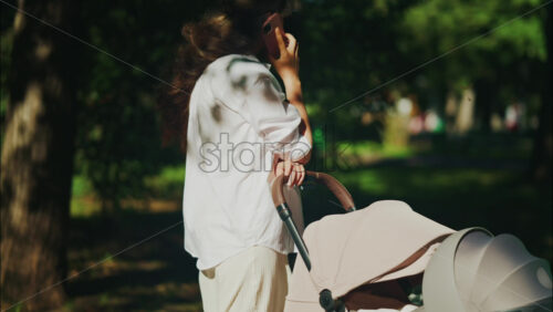 Young mother sitting on a park bench next to a stroller, enjoying a peaceful outdoor moment with her baby - Starpik Stock
