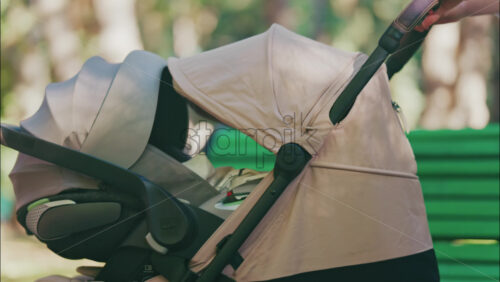 Young mother sitting on a park bench next to a stroller, enjoying a peaceful outdoor moment with her baby - Starpik Stock