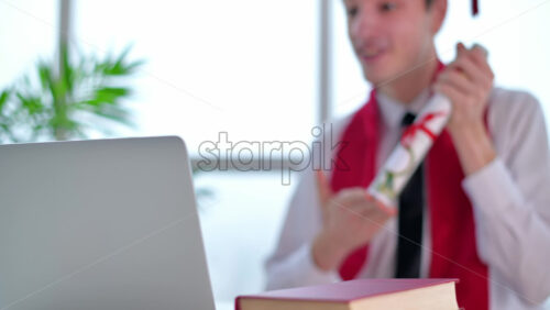 Video - Young man with graduation diploma talking towards the camera. Graduating online in virtual ceremony