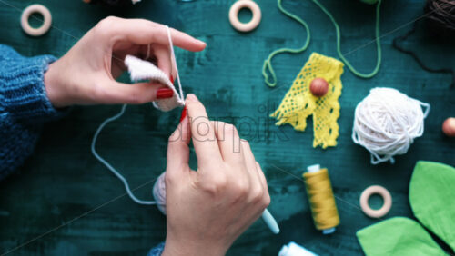 Video - Woman is knitting using hooks and white yarn above the table with equipment