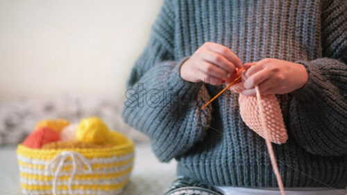 Video - Woman in gray sweatshirt is knitting a toy using hooks and pink yarn