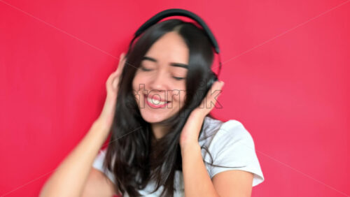 Video - Girl is listening music in headphones. Smiling. Red background