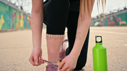 Video - Young woman tying her shoelaces at outdoors training, road. Slow motion