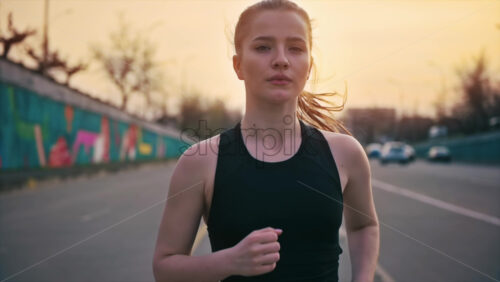 Video - Young blonde woman in sportswear running on the road at outdoors training. Slow motion, sunset