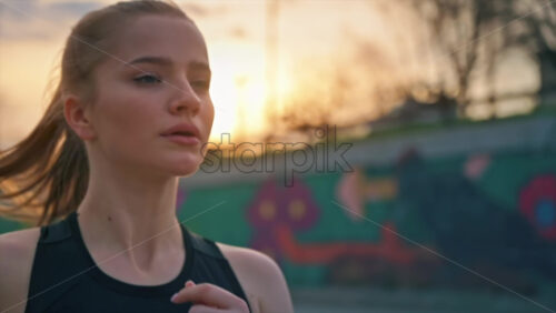 Video - Young blonde woman in sportswear running on the road at outdoors training. Slow motion, sunset