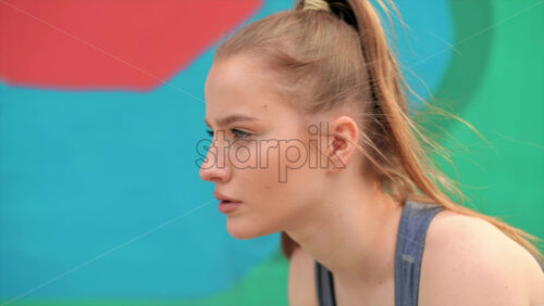 Video - Young focused blonde woman at outdoors training preparing to starting running, multicolored background. Slow motion