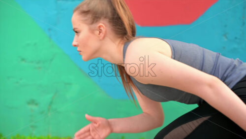 Video - Young focused blonde woman at outdoors training preparing to starting running, multicolored background. Slow motion