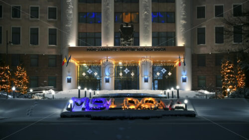 Video - Parliament of the Republic of Moldova with national emblem, illumination and Christmas decorations in the evening. Ground covered in snow. Winter in Chisinau