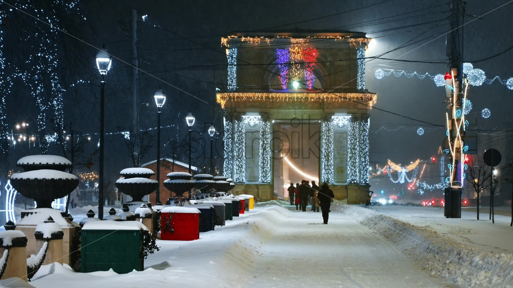 Video - People walking on Great National Assembly Square during snowfall in the evening. The Triumphal Arch in background. Christmas decorations