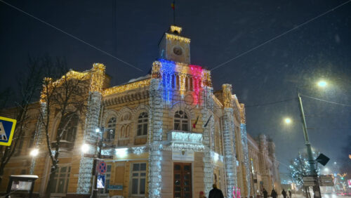 Video - Chisinau, Moldova - January 09, 2024: People walking near the City Hall with Christmas decorations during snowfall. Winter evening