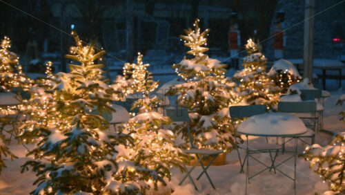 Video - Garland lamp lights on Christmas trees covered in snow near coffee tables during snowfall. Winter evening in Chisinau, Moldova