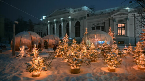 Video - Christmas trees with garland lamp lights near coffee tables during snowfall. Outdoor coffee shop. Winter evening in Chisinau, Moldova