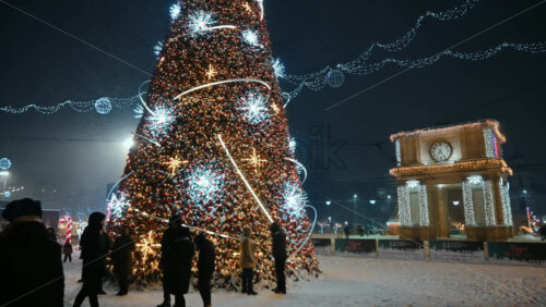 Video - Chisinau, Moldova - January 09, 2024: People talking near the artificial Christmas tree with decorations on the Great National Assembly Square during snowfall. The Triumphal Arch in background