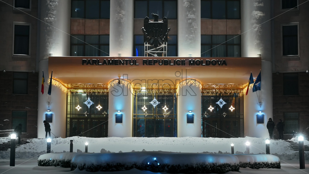 Video - Chisinau, Moldova - January 09, 2024: Parliament building with national emblem, illumination and Christmas decorations. Ground covered in snow. Winter evening