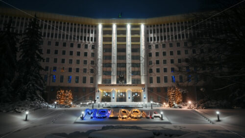 Video - Parliament of the Republic of Moldova with national emblem, illumination and Christmas decorations in the evening. Ground covered in snow. Winter in Chisinau