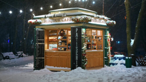 Video - Chisinau, Moldova - January 09, 2024: Illuminated Bonjour coffee shop with Christmas decorations in the central park during snowfall. Winter evening