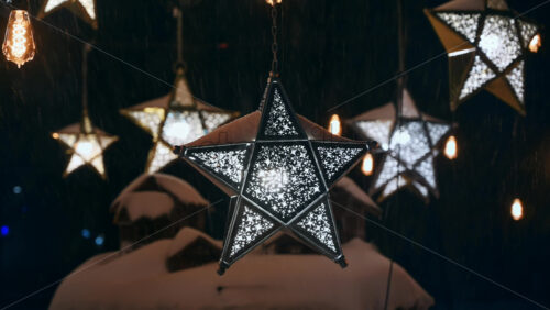 Video - Close up view of the star-shaped lanterns in the park during snowfall. Christmas decorations. Winter evening