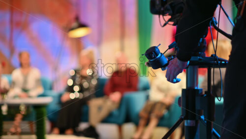 Video - Cameraman spinning focus wheel on a professional camera while filming a television talk show. Video production backstage in a dark studio