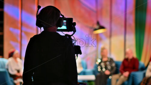 Video - Cameraman filming a television talk show on a professional camera. Video production backstage in a dark studio