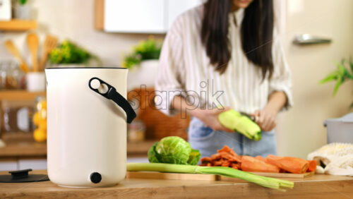Video - Young woman preparing vegetables peels for recycling in a compost bin. Housewife cooking food and composting organic waste in a bokashi container at home. Ecological and sustainability concept