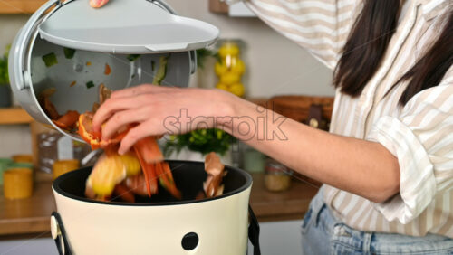 Video - Woman throwing vegetables peels in a compost bin from a collection vessel. Housewife cooking food and composting organic waste in a bokashi container at home. Ecological and sustainability concept