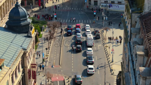 Video - Bucharest, Romania - March 03, 2024: Aerial drone view of a downtown road with moving traffic and walking people. Sunny day