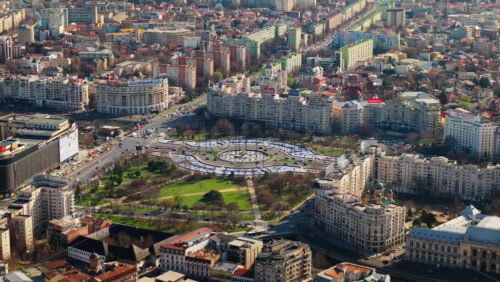 Video - Bucharest, Romania - March 03, 2024: Aerial drone view of the city downtown in sunlight. Roundabout intersection with moving cars, fountains and greenery