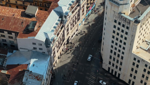 Video - Aerial drone top view of a downtown road with moving traffic and walking people in sunlight. Bucharest, Romania