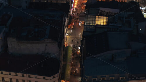 Video - Aerial drone view of walking people among old historical buildings and commercial shops in the old town in the evening. Blue hour in Bucharest, Romania