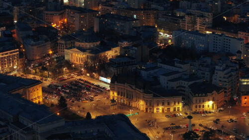 Video - Aerial drone view of Carol I University Foundation in the night. Main building with Carol I statue in front of it, roads and buildings. Illuminated Bucharest city, Romania