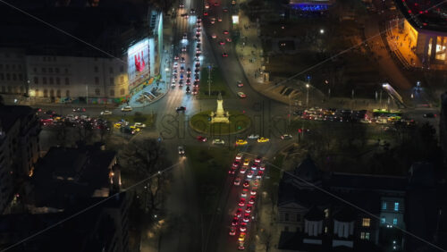 Video - Aerial drone view of a downtown roundabout intersection with moving traffic. Illuminated Bucharest in the night. Romania