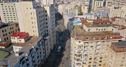 Video - Aerial drone view of a downtown road with moving traffic and walking people. Sunny day