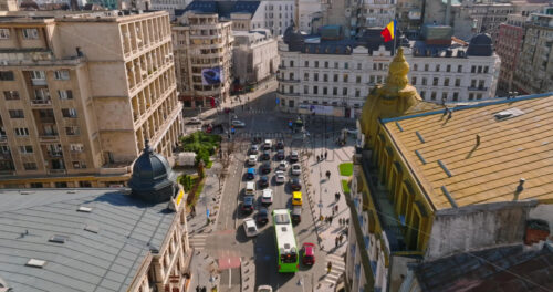 Video - Bucharest, Romania - March 03, 2024: Aerial drone view of a downtown road with moving traffic and walking people. Sunny day