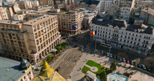 Video - Bucharest, Romania - March 03, 2024: Aerial drone view of a the city center with historical buildings, moving traffic and walking people in sunlight. Waving national flag