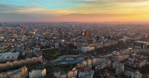 Video - Bucharest, Romania - March 03, 2024: Aerial drone view of the city downtown at sunset. Roundabout intersection with moving cars, fountains and greenery