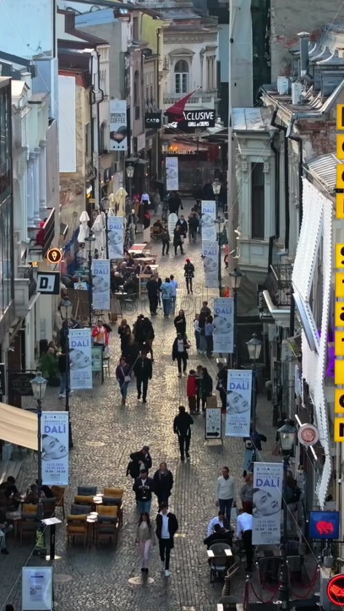 Video - Bucharest, Romania - March 03, 2024: Vertical aerial drone view of walking people among old historical buildings and commercial shops in the old town