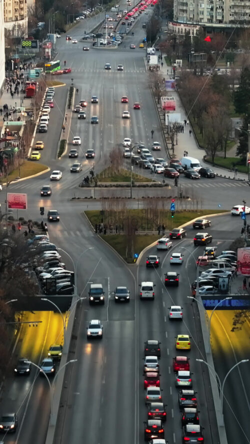 Video - Bucharest, Romania - March 03, 2024: Vertical aerial drone view of a downtown intersection with moving traffic and walking people