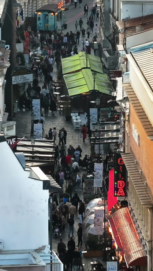 Video - Bucharest, Romania - March 03, 2024: Vertical aerial drone view of walking people among old historical buildings and commercial shops in the old town