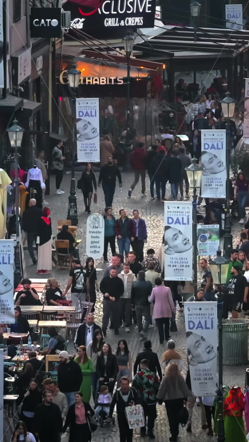 Video - Bucharest, Romania - March 03, 2024: Vertical aerial drone view of walking people among old historical buildings and commercial shops in the old town