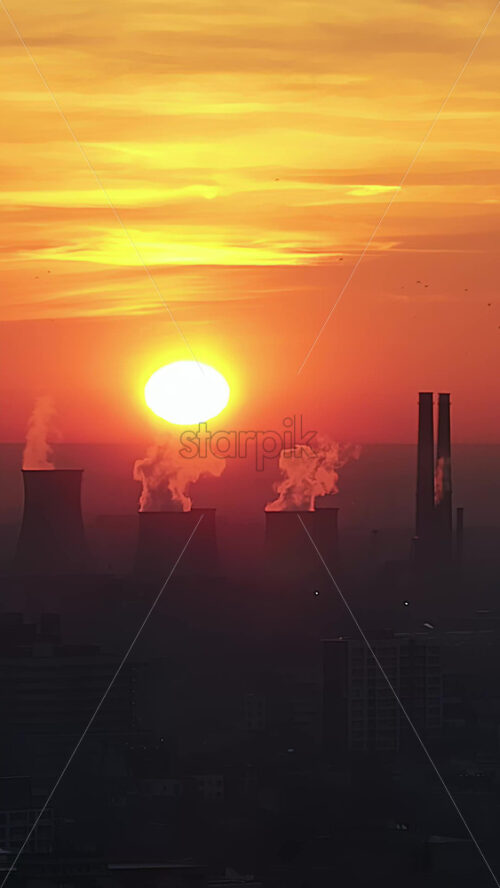 Video - Vertical aerial drone view of thermal power stations in Bucharest at sunset, red sun. Flying birds. Romania