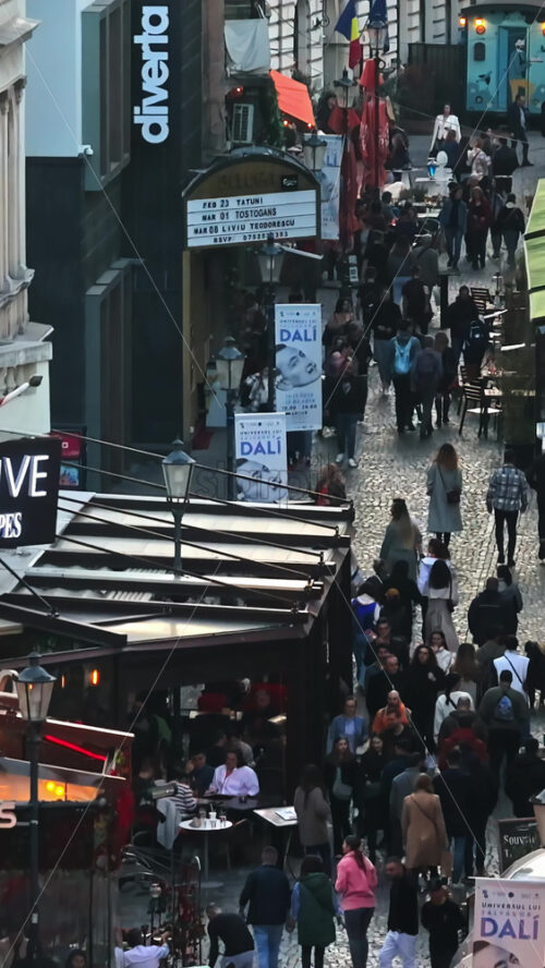 Video - Bucharest, Romania - March 03, 2024: Vertical aerial drone view of walking people among old historical buildings and commercial shops in the old town