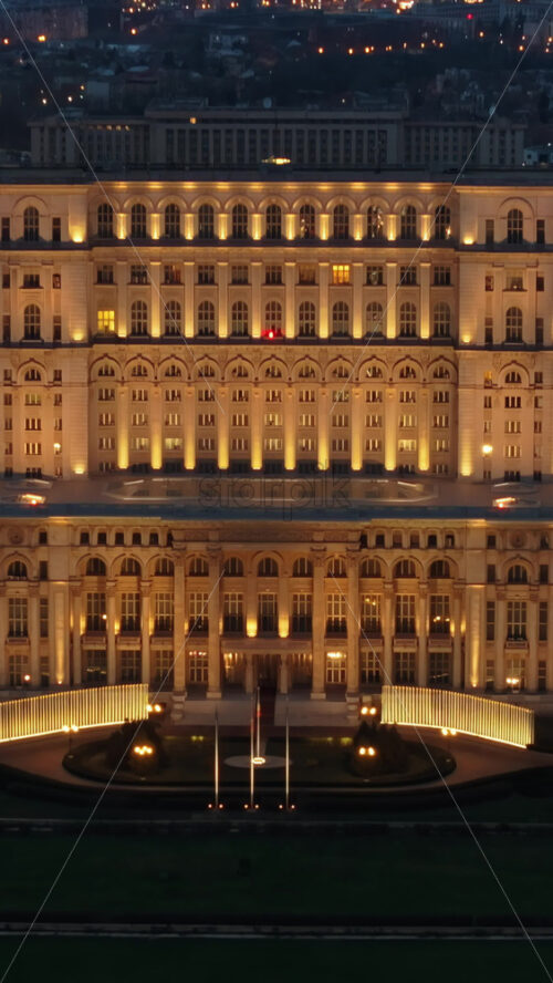 Video - Vertical aerial drone view of illuminated Palace of the Parliament in Bucharest downtown in the evening. Multiple districts around. Romania