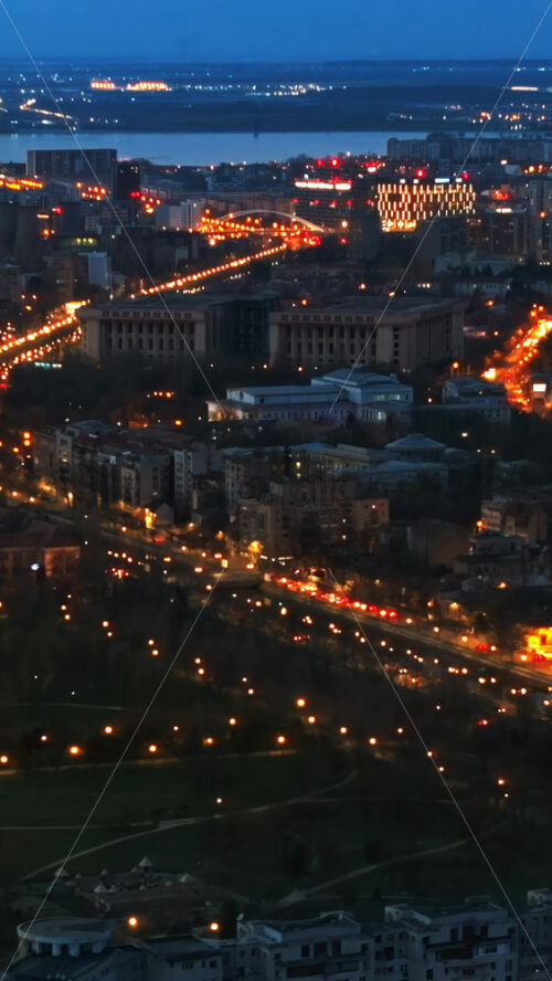 Video - Vertical aerial drone view of illuminated Bucharest cityscape in the evening. Moving traffic. Blue hour, Romania