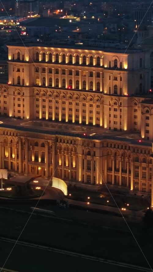 Video - Vertical aerial drone view of illuminated Palace of the Parliament in Bucharest downtown in the evening. Multiple districts around. Romania