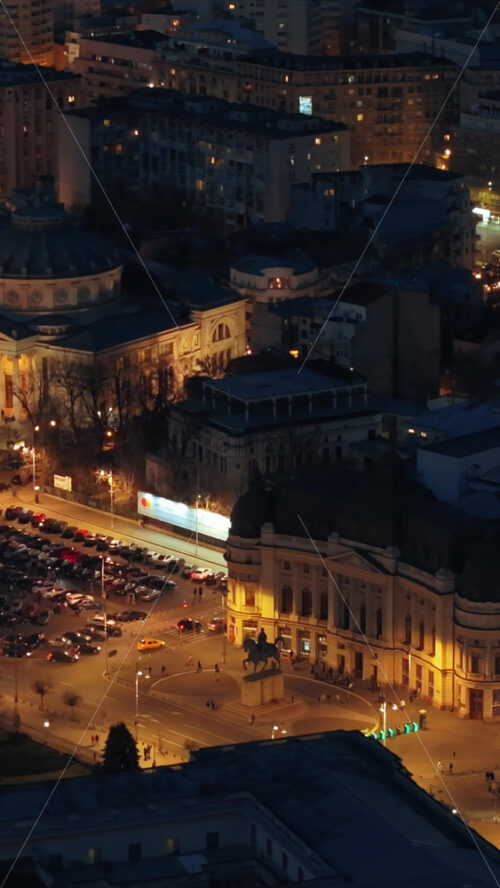Video - Vertical aerial drone view of Carol I University Foundation in the night. Main building with Carol I statue in front of it, roads and buildings. Illuminated Bucharest city, Romania
