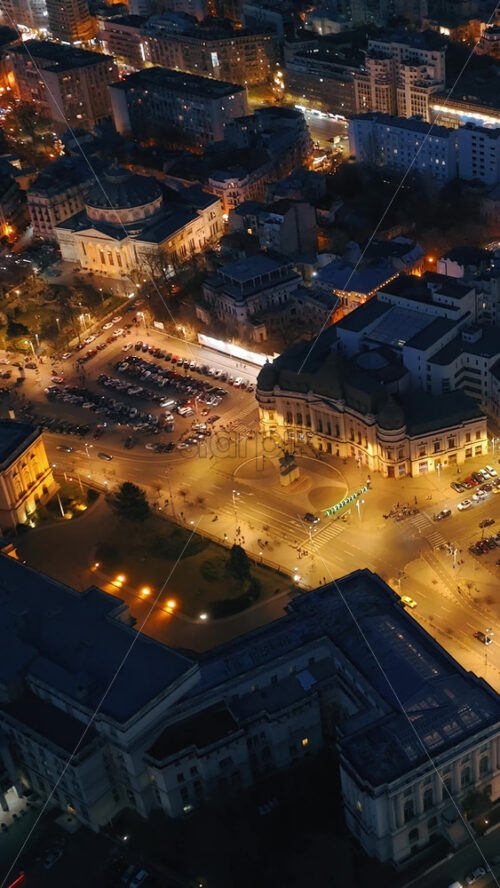 Video - Vertical aerial drone view of Carol I University Foundation in the night. Main building with Carol I statue in front of it, roads and buildings. Illuminated Bucharest city, Romania
