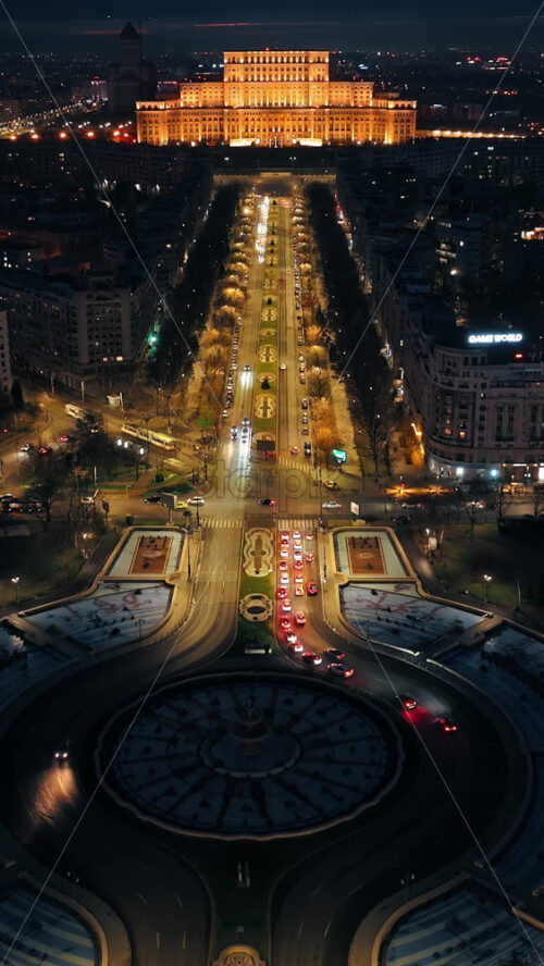 Video - Bucharest, Romania - March 03, 2024: Vertical aerial drone view of the city downtown. Roundabout intersection with moving cars and fountains. Palace of the Parliament in the distance