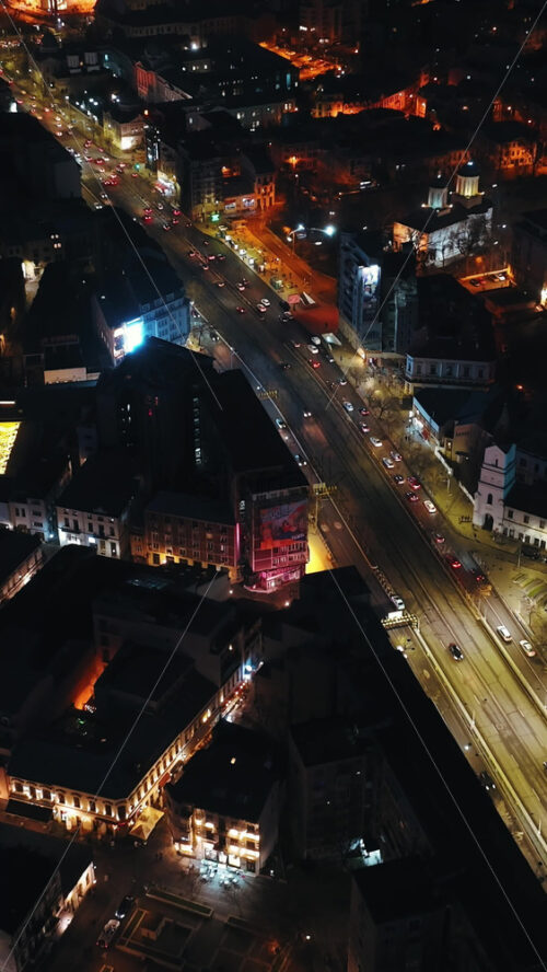 Video - Bucharest, Romania - March 03, 2024: Vertical aerial drone view of illuminated cityscape in the night. Moving traffic on the road