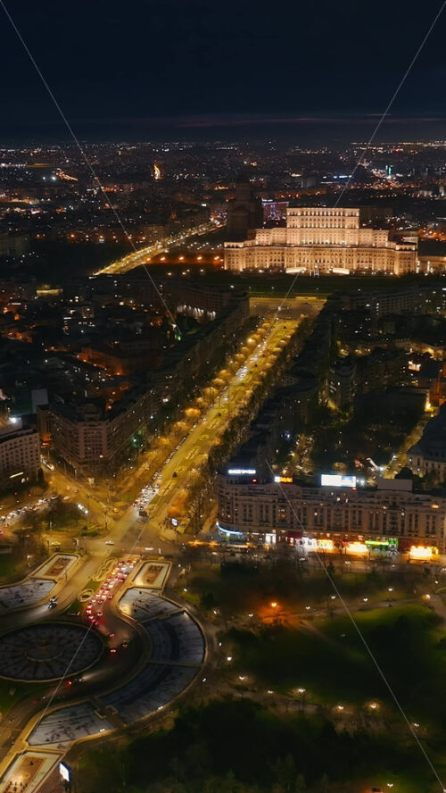 Video - Vertical aerial drone view of illuminated Palace of the Parliament in city downtown in the night. Multiple districts around in Bucharest, Romania