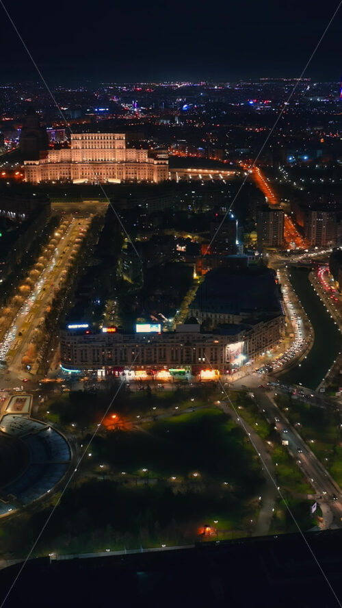 Video - Vertical aerial drone view of illuminated Palace of the Parliament in city downtown in the night. Multiple districts around in Bucharest, Romania